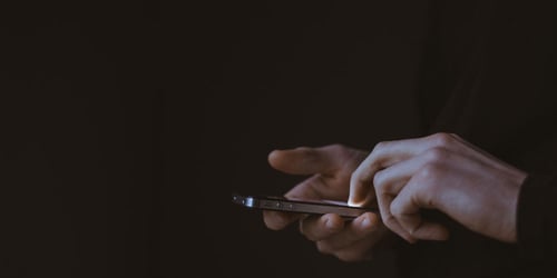 Someone with only their hands in view is scrolling on their phone with a brightly lit screen.